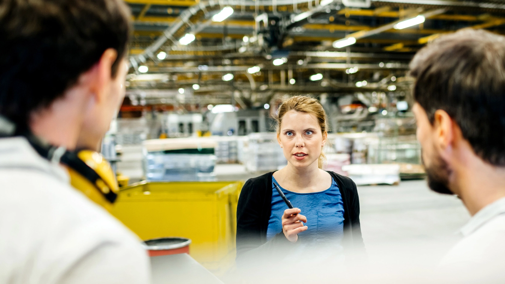 Eine Frau spricht mit zwei Männern an einer Produktionslinie.
